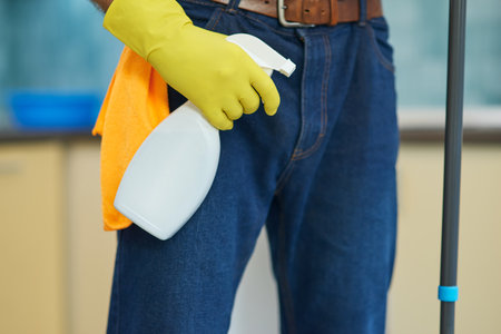 All surfaces clean. Close up of professional male cleaner wearing gloves and holding spray detergent while cleaning a kitchenの写真素材