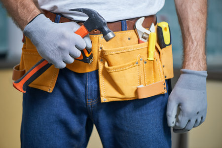 Ready to fix anything. Close up of repairman wearing a tool belt with various tools, holding a hammer in his handの写真素材