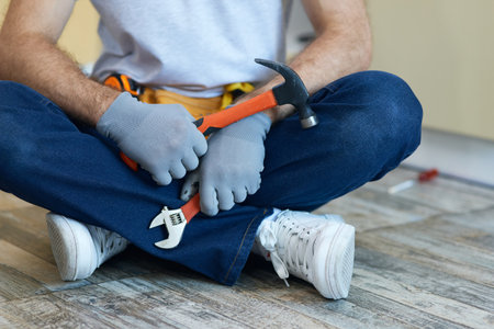 Quality repair. Cropped shot of young repairman holding a hammer and an adjustable wrench in his hands while sitting on the floor indoorsの写真素材