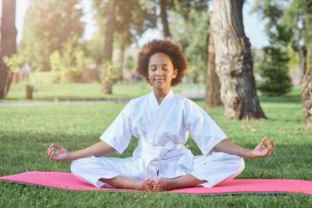 Cute Afro American girl in karate kimono meditating outdoorsの写真素材