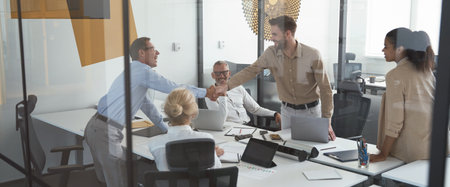 Two successful businessmen shaking hands while having a meeting with colleagues in conference room in the modern officeの写真素材