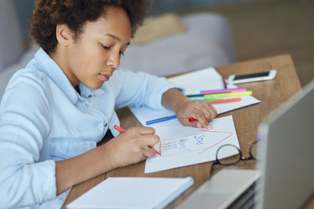 Portrait of focused teen schoolgirl using markers while doing her homework with laptop computer at homeの写真素材