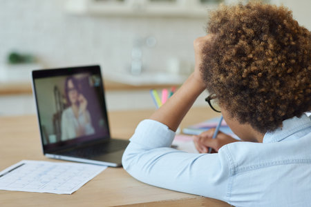 Rear view of mixed race teen schoolgirl drawing on paper with marker, using laptop while having online video lesson with teacher, sitting at homeの写真素材