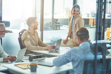 Young cheerful mixed race female office worker discussing something with colleagues while sitting in board room in the modern office, business people having a meetingの写真素材