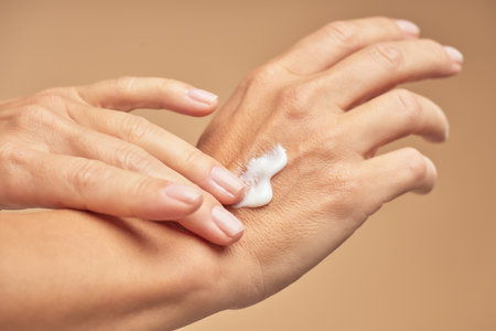 Female hands with nude manicure on nails applying hand creamの写真素材