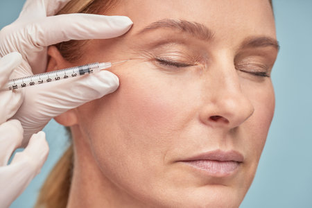 Close up portrait of a beautiful mature woman keeping eyes closed while receiving hyaluronic acid injection by beauticianの写真素材