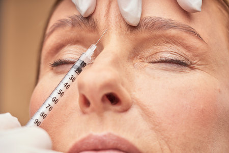 Anti Aging procedures. Close up shot of beautician in protective gloves making cosmetic injection in female foreheadの写真素材