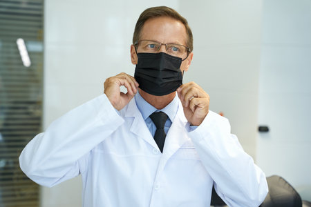 Mindful medical doctor covering his face with protective maskの写真素材
