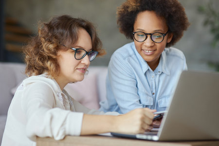Portrait of attractive female teacher helping her little student, teen schoolgirl with homework, sitting at the table at homeの写真素材