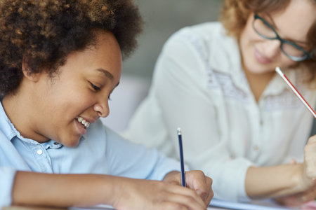 Learning is fun. Close up shot of mixed race teen girl looking concentrated while writing with pencil during a lesson with her female teacherの写真素材