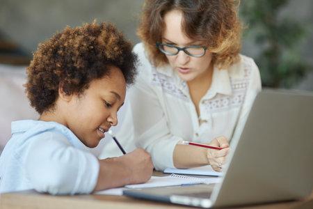 Commitment to excellence. Enthusiastic mixed race teen schoolgirl writing during a lesson with her female teacher at homeの写真素材