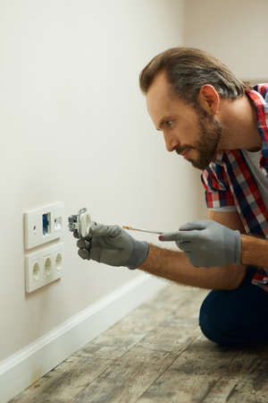 Quality work every time. Portrait of electrician wearing protective gloves, using a screwdriver...