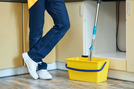 Cleaned right. Cropped shot of professional male cleaner standing next to the bucket with mop, ready for cleaning floor at homeの写真素材
