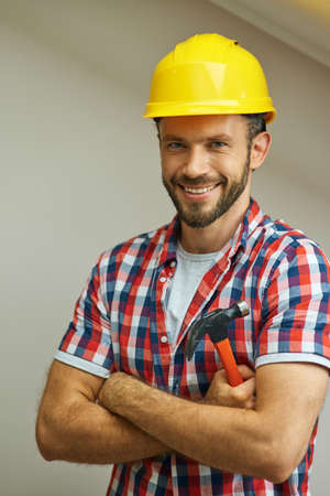 Portrait of joyful handyman wearing a helmet smiling at camera, standing with arms crossed and...