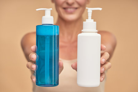 Happy woman holding bottles with natural skincare product in studioの写真素材