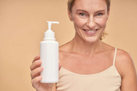 Close up of smiling beautiful woman holding moisturizing body creamの写真素材