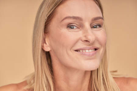 Feeling so beautiful. Portrait of a happy middle aged woman with clean skin and smiling at camera while posing over beige backgroundの写真素材