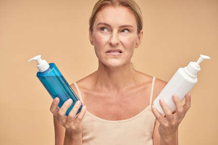 Mature lady holding two bottles of cream isolated on beige backgroundの写真素材