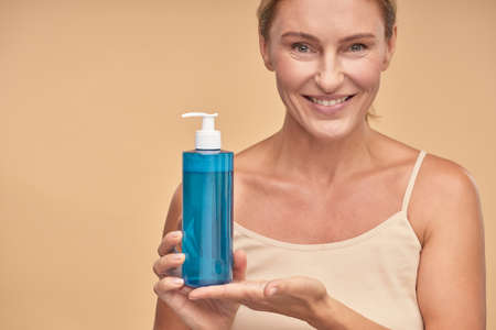 Smiling lady holding micellar water in bottle in studioの写真素材