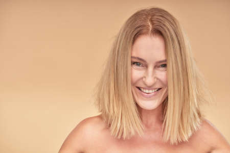 Portrait of attractive mature woman smiling at camera while posing over beige backgroundの写真素材