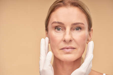 Cosmetology and skincare concept. Beautician hands in white gloves checking female face skin before medical therapyの写真素材