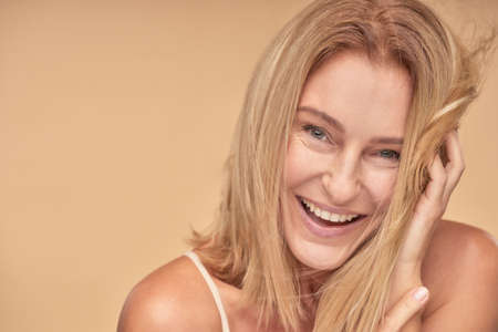 Happy pretty mature woman posing while touching hair by handsの写真素材