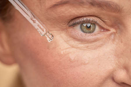 Mature woman moisturizing the skin near the eyes with a special serumの写真素材