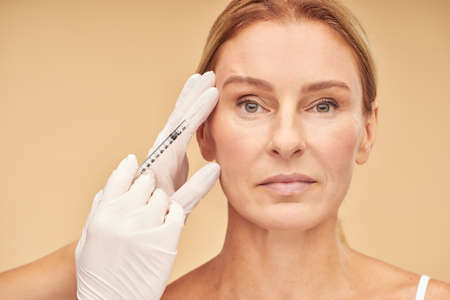 Anti aging procedures. Beautiful mature woman receiving hyaluronic acid injection by beauticianの写真素材