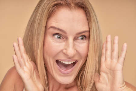 Close up portrait of excited mature woman with surprised look over beige backgroundの写真素材