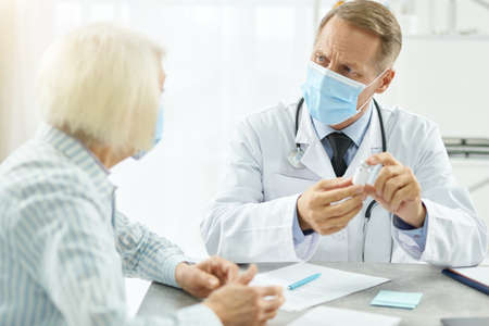 Male doctor in medical mask discussing vaccine with patientの写真素材