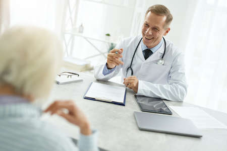 Cheerful male doctor talking with elderly woman in his officeの写真素材