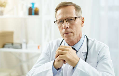Highly qualified doctor sitting at the table in clinicの写真素材