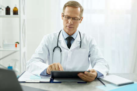 Handsome doctor using modern tablet computer at workの写真素材