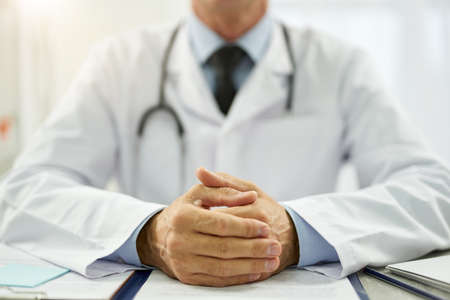 Male doctor putting hands on table with documentsの写真素材