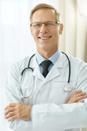 Cheerful male doctor in lab coat standing in clinicの写真素材