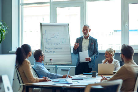 Confident mature businessman giving a presentation, explaining something to colleagues while having a meeting in the officeの写真素材
