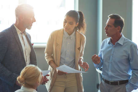 Group of multiracial business people discussing project results, analyzing reports while having a meeting in the modern officeの写真素材