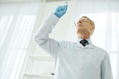 Highly qualified doctor in lab coat holding bottle of vaccineの写真素材