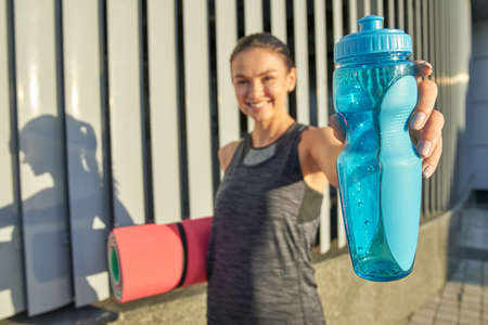 Selective focus on bottle with water in fitness girl hand