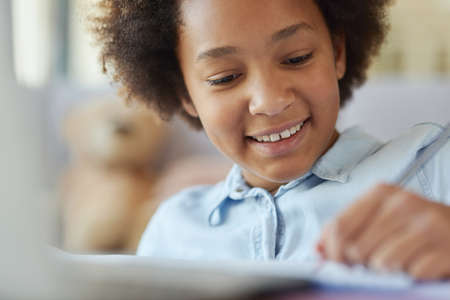 Close up shot of mixed race teen girl looking happy while doing homework, spending time at home