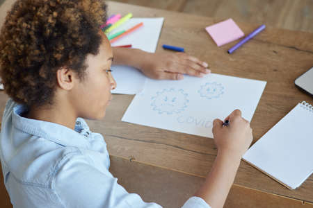 Mixed race teen schoolgirl drawing on paper with colorful markers while spending time at home during quarantineの写真素材