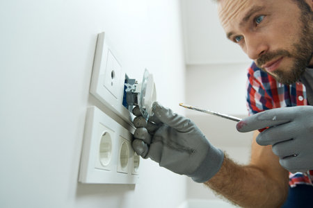 Installation process. Close up shot of electrician wearing protective gloves looking focused while installing new plug socket in a houseの写真素材