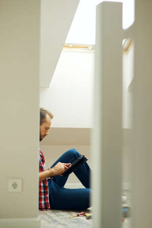 Repairman using digital tablet while sitting on the floor and taking a break. Home repair hand tools on laminate flooringの写真素材