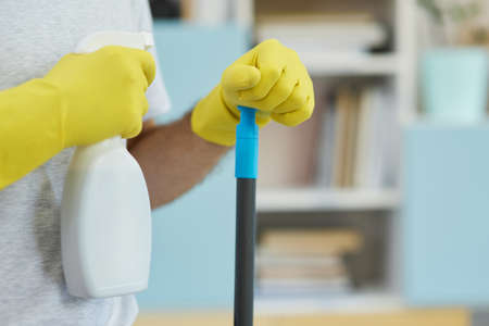 Safe and clean. Close up shot of professional male cleaner wearing gloves, holding spray detergent and mop while getting ready for cleaning a kitchenの写真素材