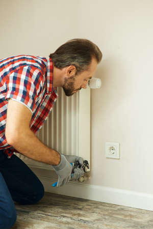 Quality help. Handyman using pipe wrench while repairing radiator battery in the room. Heating restorationの写真素材