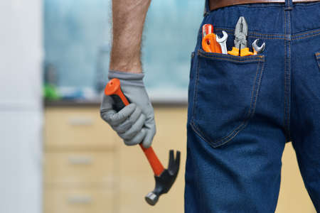 Nail it. Close up shot of various plumbing hand tools in mans jeans back pocket. Professional repairman holding a hammer, standing indoorsの写真素材