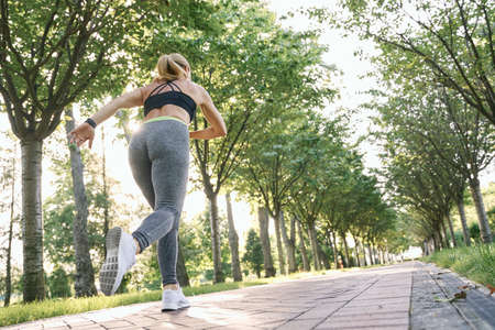 Keep moving. Rear view of sportive woman in sportswear starting to run while training in green park on sunny dayの写真素材