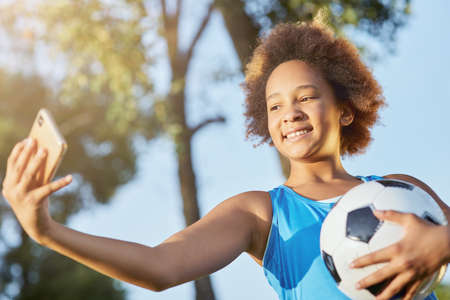Cute little girl with soccer ball making selfie outdoorsの写真素材