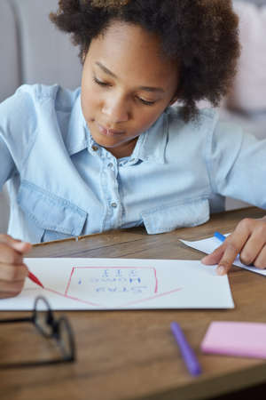 Mixed race teen schoolgirl drawing on paper with colorful markers while spending time at home during quarantineの写真素材
