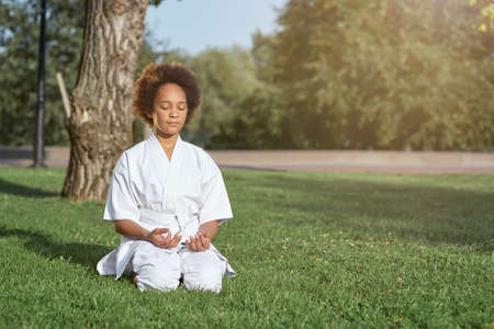 Adorable little girl in karate kimono meditating outdoorsの写真素材